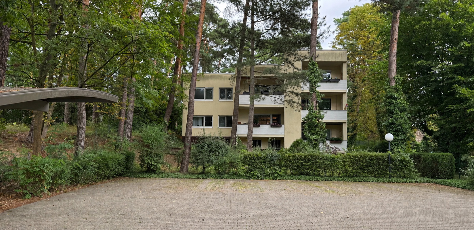 KI-bearbeitete Außenansicht des Mehrfamilienhauses im alten Baumbestand, ohne parkende Fahrzeuge