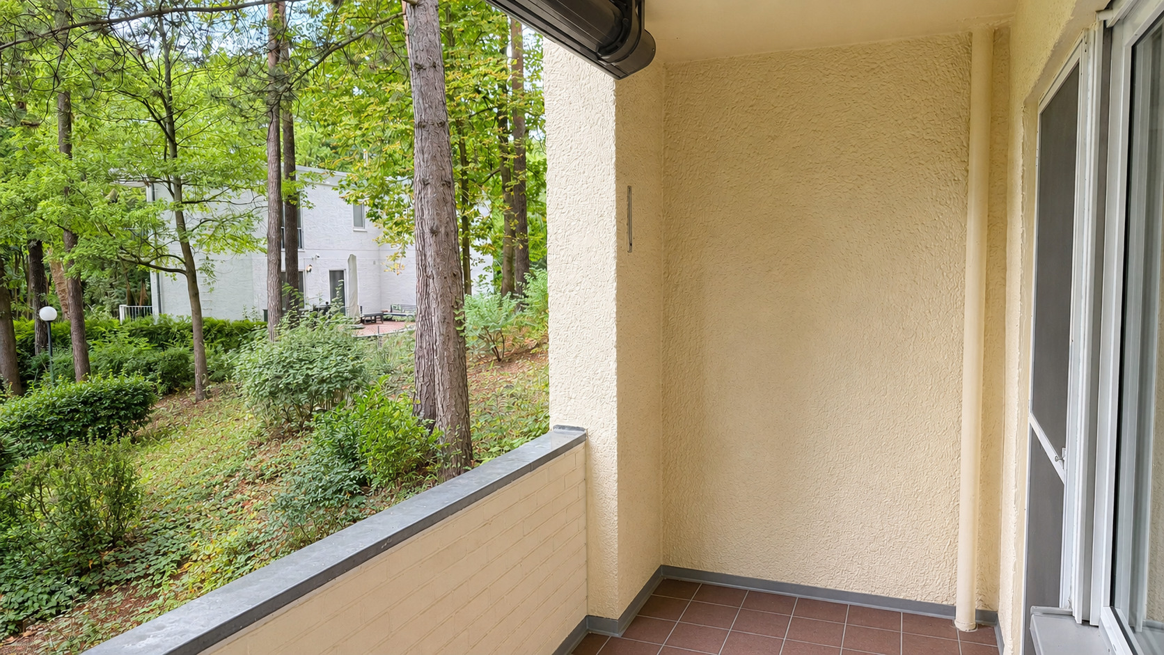 KI-bearbeitete Darstellung der leer geräumten Loggia mit Blick in die grüne Wohnanlage